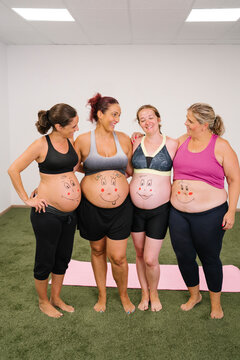 Smiling group of pregnant woman with face drawing on stomach standing at yoga studio