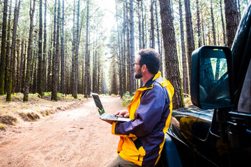 Mature man using laptop while leaning on car in forest at El Teide National Park, Tenerife, Spain