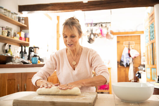 Senior woman preparing dough while sitting in kitchen