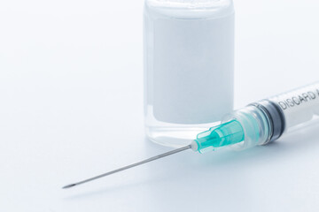 A hypodermic needle next to a vial containing a vaccine