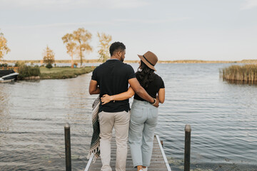 Boyfriend and girlfriend with arm around walking on pier against lake