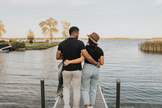 Fototapeta Boyfriend and girlfriend with arm around walking on pier against lake