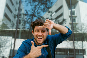 Cheerful businessman making finger frame against modern glass building