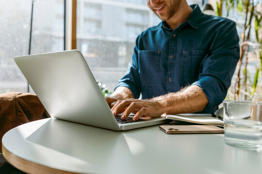 Smiling Young Businessman Working On Laptop At Table In Cafe