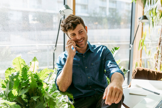 Smiling young businessman talking on smart phone while sitting in cafe