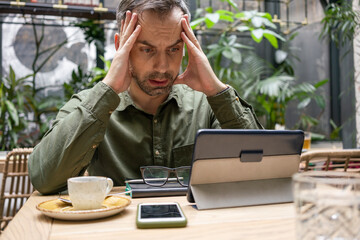 Businessman with head in hands using digital tablet while sitting at cafe