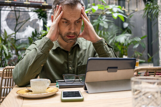 Businessman with head in hands using digital tablet while sitting at cafe