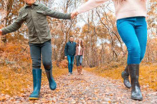 Low section of sibling holding hands running while parents standing behind in park during autumn