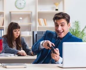 Man playing games in office while colleague is busy