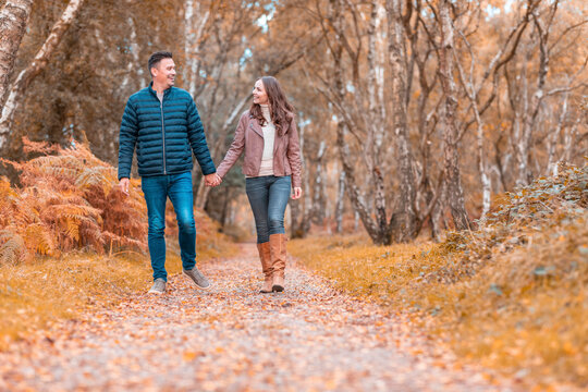 Happy heterosexual couple holding hands walking in park during autumn