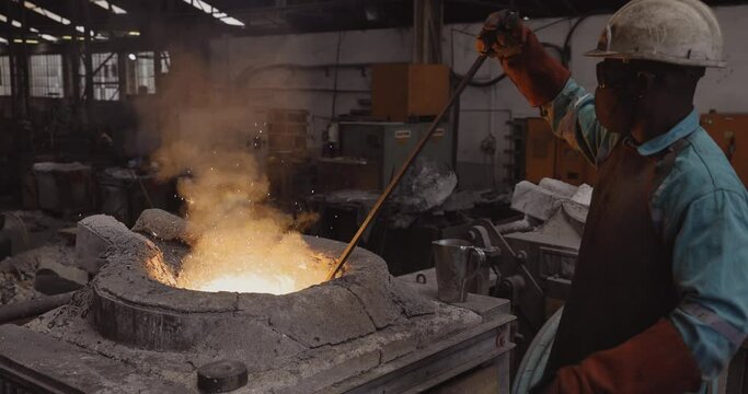 Factory worker stiring up metal in a smelting furnace at a steel foundry
