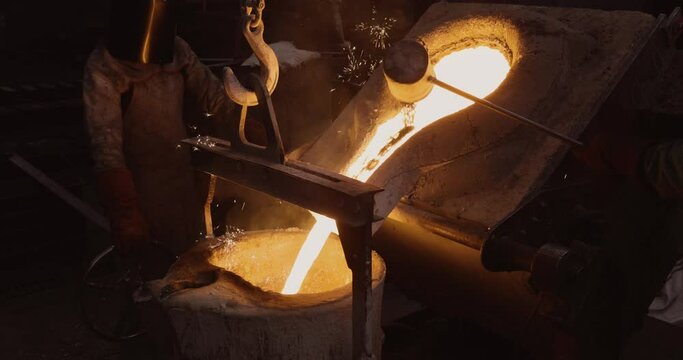 Close-up view of a factory worker pouring molten metal out a smelting furnace at a steel casting foundry