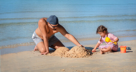 dad and daughter are building a sand castle on the beach