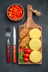 Vertical view of tasty cutlets chopped vegetables greens for dinner on dark background