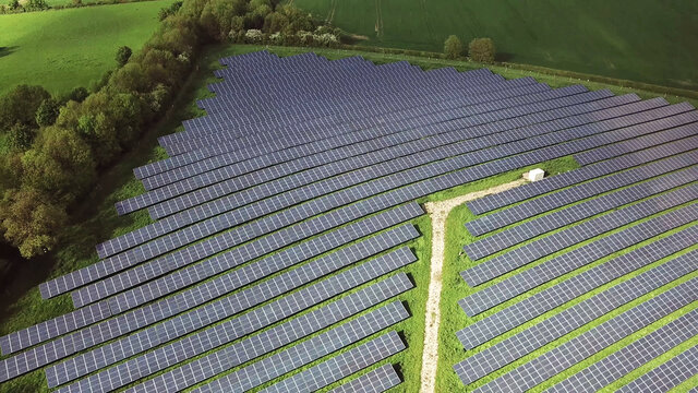 Solar panels cells in solar energy farm between green fields.