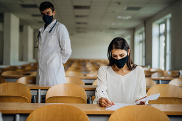 Female student taking an exam wearing a protective face mask in an empty amphitheater. Stressed student during COVID-19 outbreak.Coronavirus in-class test. Concerned woman having education evaluation