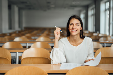 Knowledgable smiling student taking an easy exam in an empty amphitheater. An optimistic student taking an in-class test. Happy woman having stress free education evaluation.Essay exam inspiration.