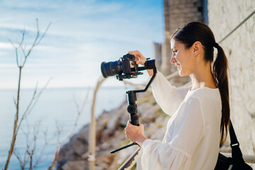 Smiling female travel vlogger video creator filming with a mirrorless camera on a gimbal stabilizer.Freelancer woman recording a low budget film for a vlog.Social media influencer online video stream
