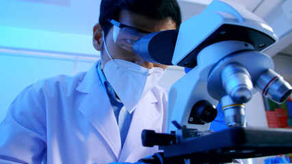 Asian scientist doing some research and looking through a microscope in laboratory.