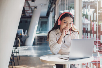 Young Asian woman student sitting in café while using laptop computer and listening music.
