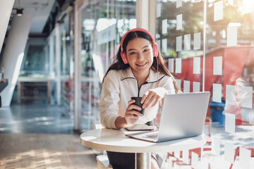 Fototapeta premium Young Asian woman student sitting in café while using laptop computer and listening music.