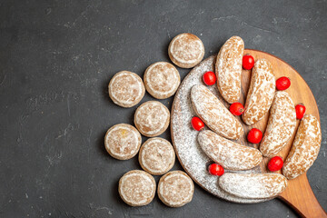 Top view of delicious cookies on a brown cutting board with red cornell berries on dark background