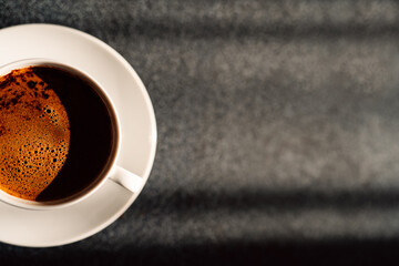 Cup with aromatic hot coffee.Creamy cup of black coffee.Classic filter arabica drink.Espresso americano.Favorite hot beverage.Morning sunrays on the table.Caffeine energy.Gray copy space.