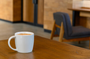 white coffee cup with hot cappuccino coffee on wooden table in coffee cafe. copy space for adding text