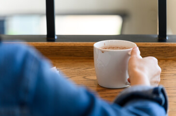 Back view of female hands holding a coffee cup in modern coffee shop, woman drinking coffee during recreation time