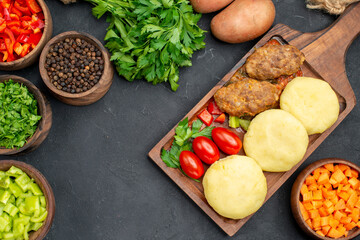 Top view of tasty cutlets with vegetables and a bunch of green on dark background