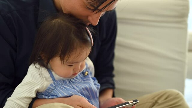 スマートフォンで動画を楽しむ赤ちゃんとお父さん