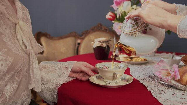 close up frame of a vintage mug on a red tablecloth which is slowly filled with tea