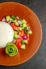 Half shot of homemade rice dish for dinner and salad with tomato and cucumber on dark background