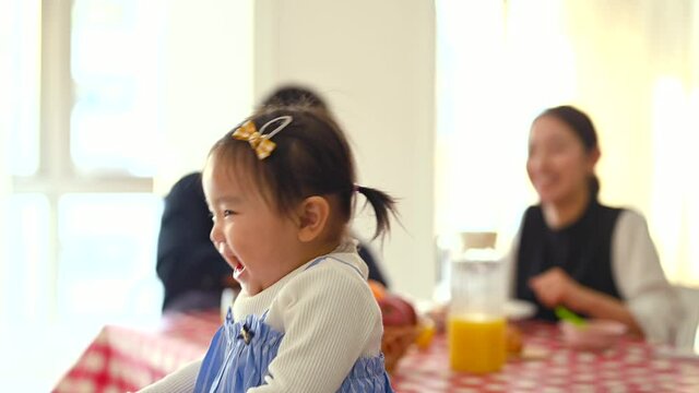 両親が食事をしながら椅子の上で遊ぶ赤ちゃんを見守っている。