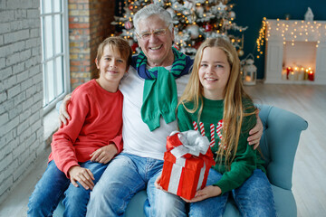 Obraz na płótnie Canvas Grandfather and grandchildren in a room decorated for Christmas against the background of a Christmas tree. Christmas holiday concept. contrast photography. High quality photo.