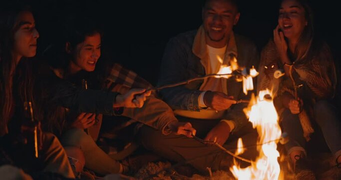 Group of friends eating marshmallows on bonfire at night