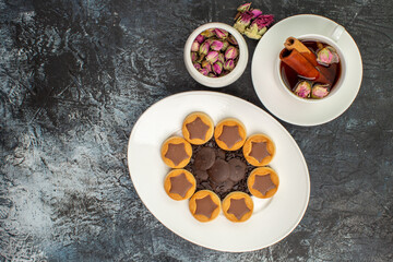 top view of cookies on white plate with a cup of herbal tea with a bowl of dry flower on grey ground