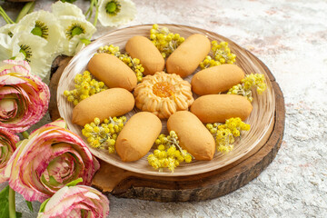 a plate of sweet cookies on wooden platter and beautifeul-colored flowers on white marble ground