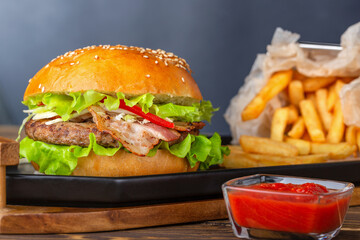Burger with bacon, meat, tomato and lettuce with french free on wooden modern plate.