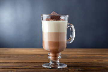 Glass of hot chocolate  of three layered drink on wooden table. Cacao, caffeine.