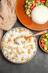 Homemade rice dishes and salad with tomato and cucumber and towel on dark background
