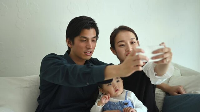 赤ちゃんと若い夫婦がスマートフォンで自撮りをしている