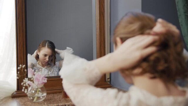 girl gently braids her hair looking in a vintage mirror