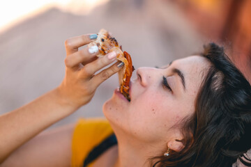 Mujer comiendo pizza, Lunch time concept. Attractive cheerful woman eats delicious Italian pizza, surprised with wonderful taste, indicates with thumb aside, shows where pizzeria situated, suggests to