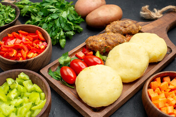 Horizontal view of tasty cutlets with vegetables and a bunch of green on dark table