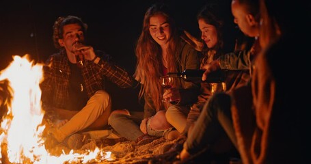 Friends drinking pouring wine bottle at beach bonfire at night
