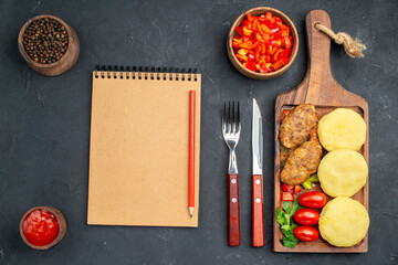 Top view of tasty cutlets chopped vegetables greens for dinner and notebook on dark background