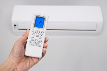 Man's hand using remote control open The air conditioner is cooled to 25 degrees Celsius in his bedroom. Health concepts and energy savings.soft focus