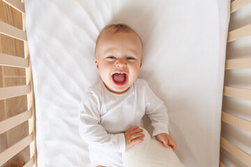 Funny blond cute baby lying and laughing in white children bed