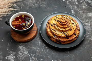 Above view of homemade pancakes with chocolate and a cup of cinammon tea on gray background